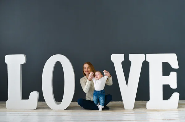 Portrait  happy mother and baby,on gray background near large letters of the word love