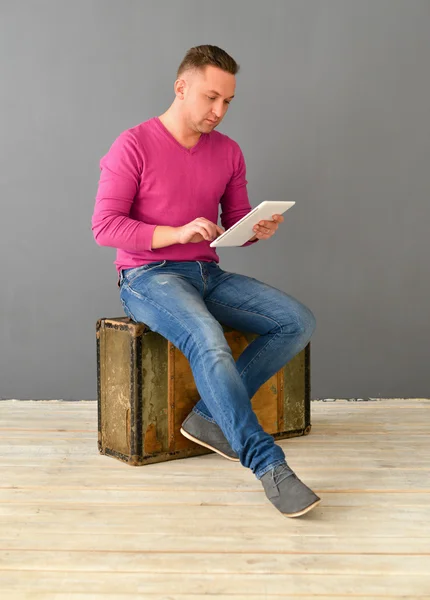Attractive young man  sits on an old suitcase and holding plane-table