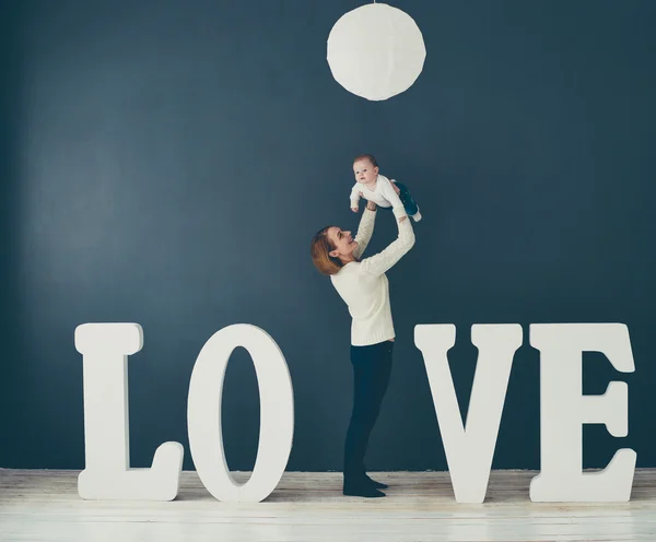 Portrait  happy mother and baby,on gray background near large letters of the word love