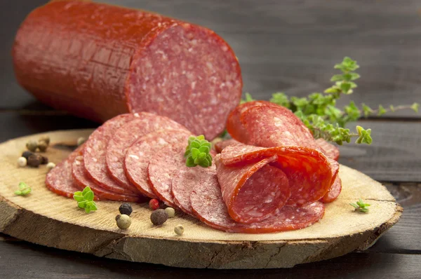 Halved in slices turkey salami served on a slice of wood with thyme and ground pepper