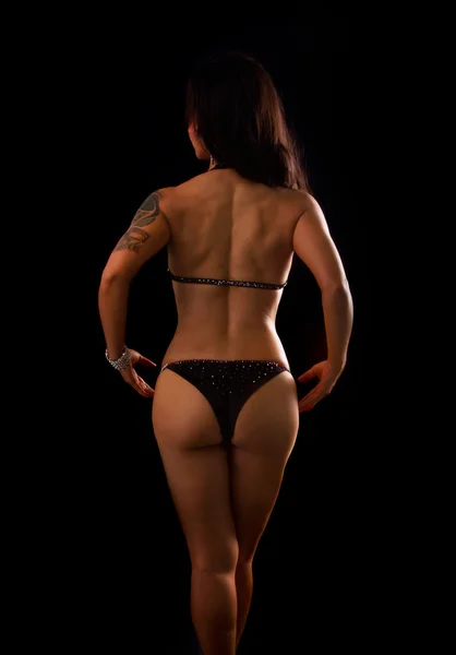 Athletic asian woman showing muscles of the back  on a black bac