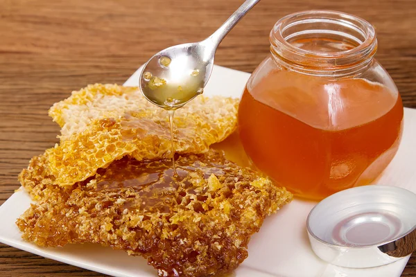 Spoon with a pouring drop of golden honey on honey comb