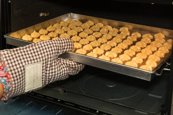 Woman hand putting a tray of raw pastry in the oven