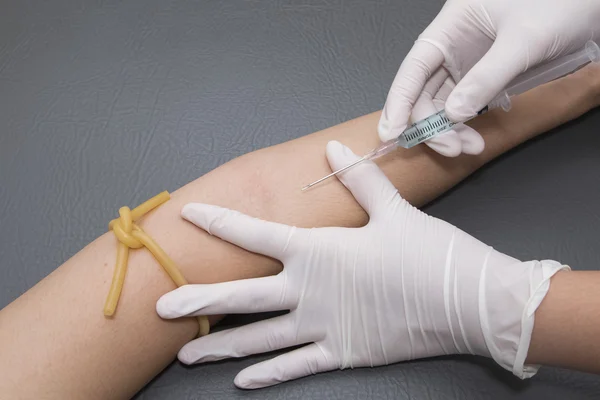 Woman arm with a tourniquet getting injection with a syringe at