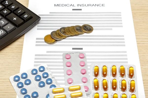 Coins, pills and calculator laying on the blank of medical insur