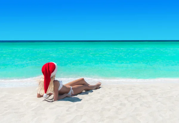 Woman in Christmas Santa hat sunbathing at tropical ocean beach
