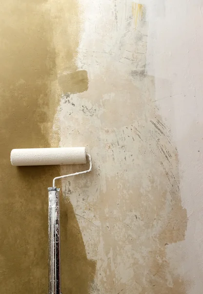 Paint roller applying paint on white wall, home improvements