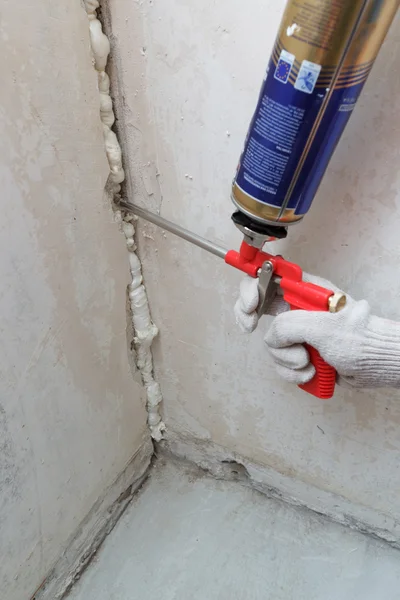 Worker\'s hand fix a rent in wall using polyurethane foam