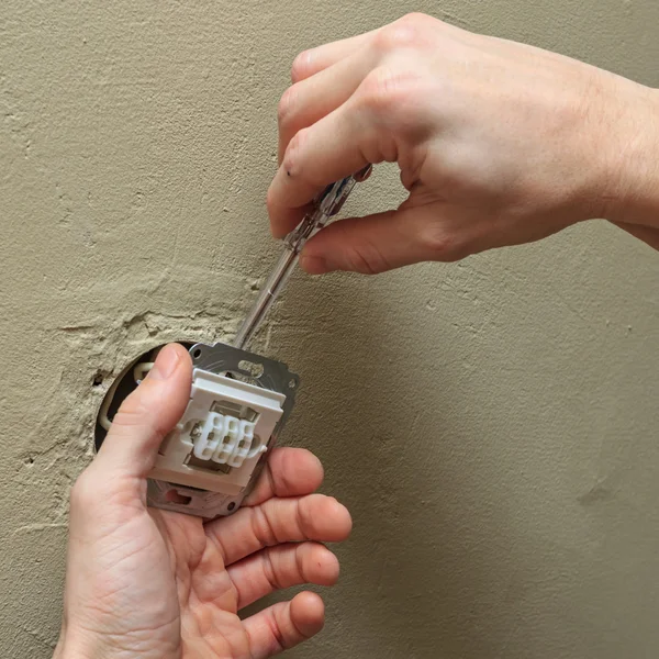 Electrician hands with screwdriver installing light switch in wall