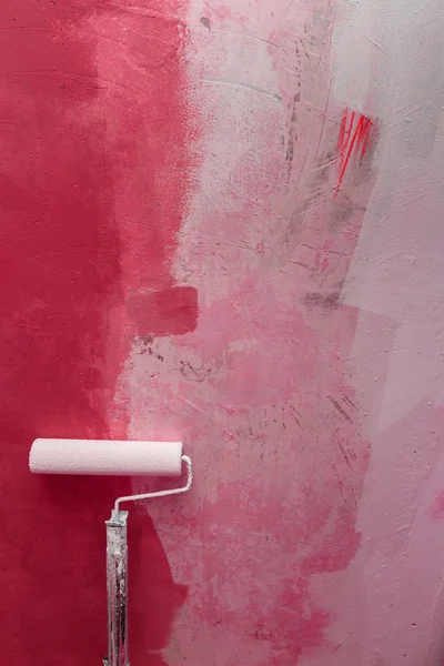 White paint roller and red paint on white wall