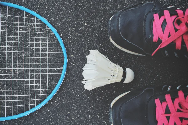 Selfie of sport shoes and shuttlecocks with badminton racket.