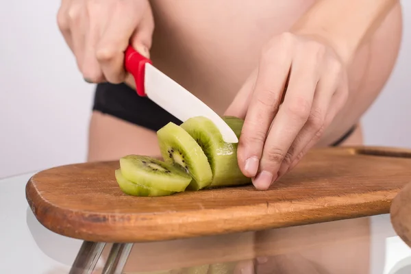 Portrait of pregnant mother cuts kiwi fruit