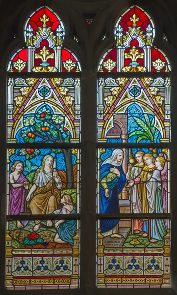BRUGES, BELGIUM - JUNE 12, 2014: Scenes Sarah and the vistitation of God to Abraham and the Little st. John the Baptist and Jesus on the windwopane in st. Jacobs church by J. Dobbelare (1901).