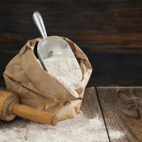 Rye flour in brown paper bag on wooden background.