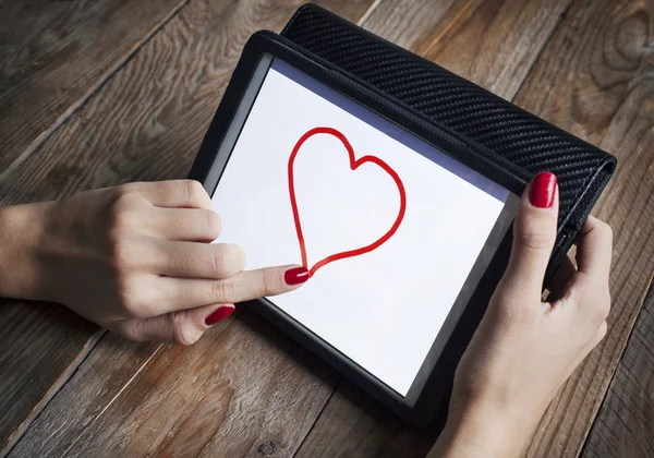 Young girl draws heart on the tablet