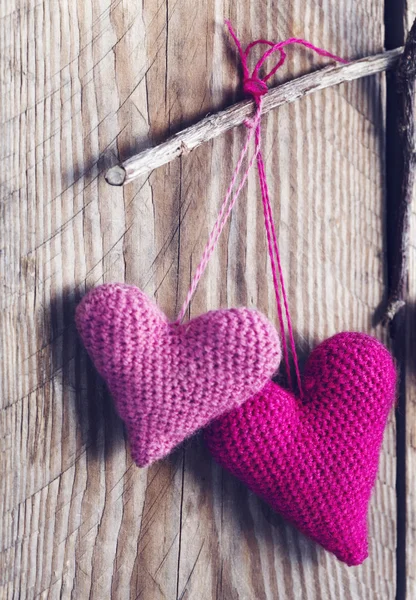 Crochet pink hearts on wooden background.