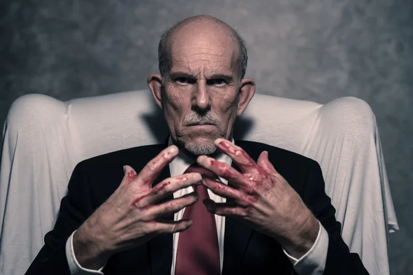 Bad businessman with bloody hands sitting in white chair. Gray b