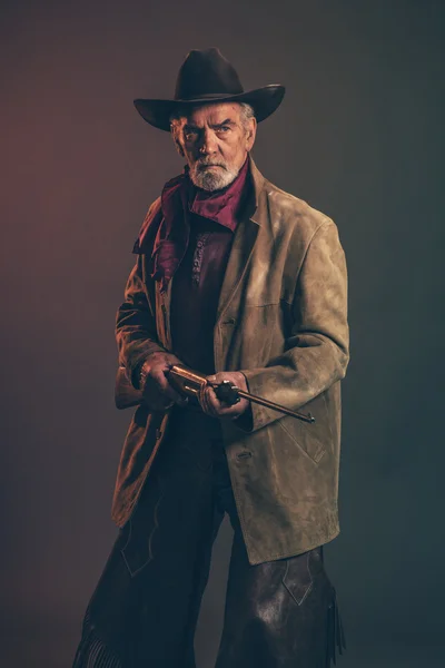 Old rough western cowboy with gray beard and brown hat holding r