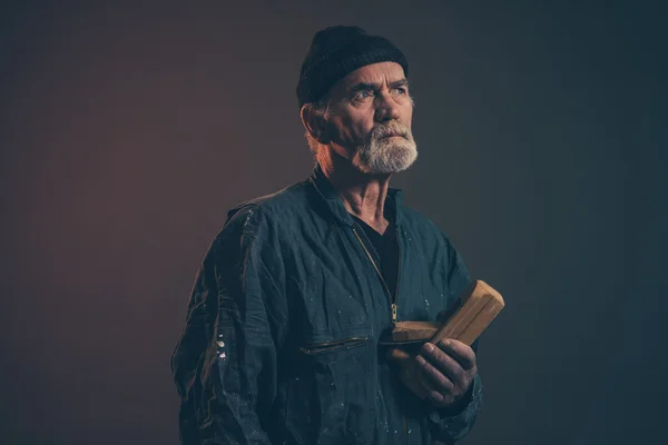 Senior carpenter with gray hair and beard holding old plane wear