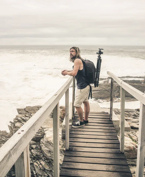 Man with long blonde hair standing on wooden bridge at Tsitsikam