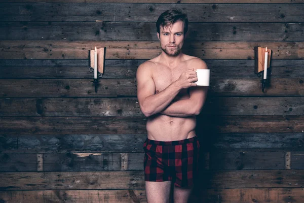 Man with blonde hair and bare chest wearing red flannel shorts.