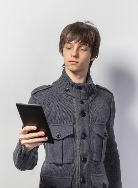 Portrait of a cool young guy standing in casual clothes, holding on digital tablet while standing on white background
