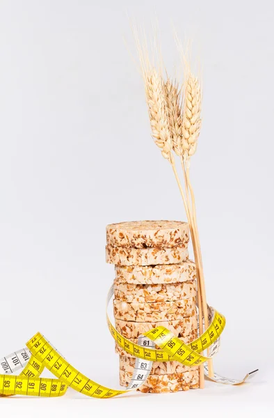 A yellow measuring tape wrapping sheaf of wheat and rice cakes - healthy eating concept