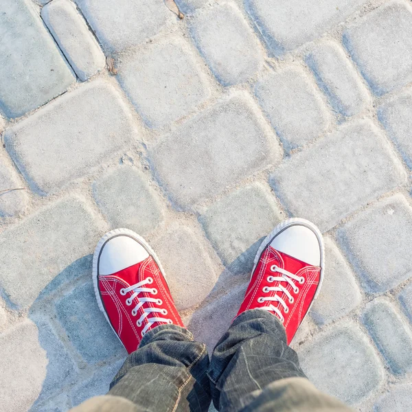 Young man feet in red sneakers on cobbled road