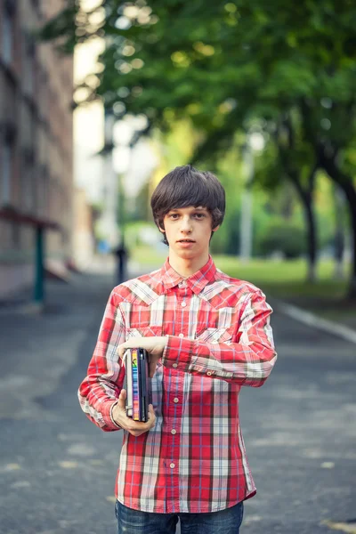 Young student man holding a book and tablet against a city background
