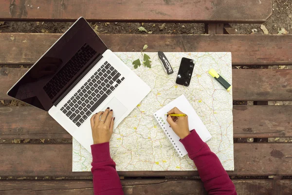 Planning travel on wood table outside with map, laptop, knife, n