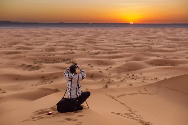 Photographer behind tripod on sand dune is silhouetted by settin