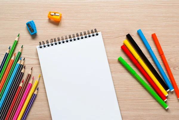 Pencils, crayons and notebook on a desk.