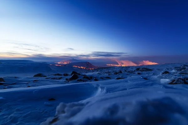 Snow-covered mountainside, night photo. In the distance the steel mills.