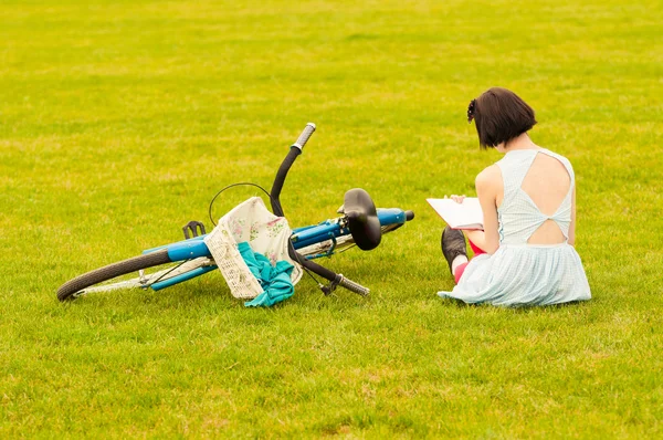 Beautiful young woman in dress sitting on grass with a book