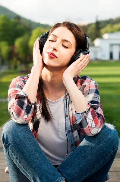 Peaceful hipster female enjoying music outside in the park