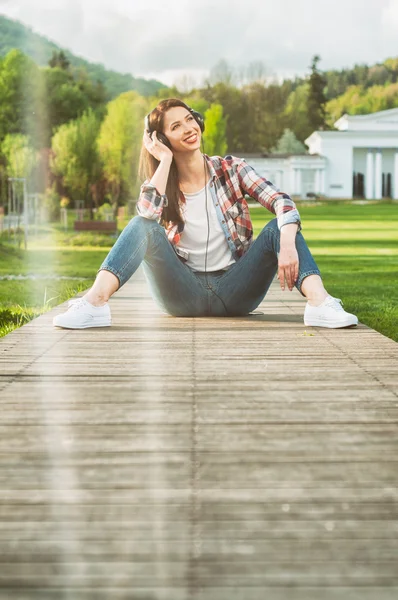Young female in casual outfit sitting outside and listening musi