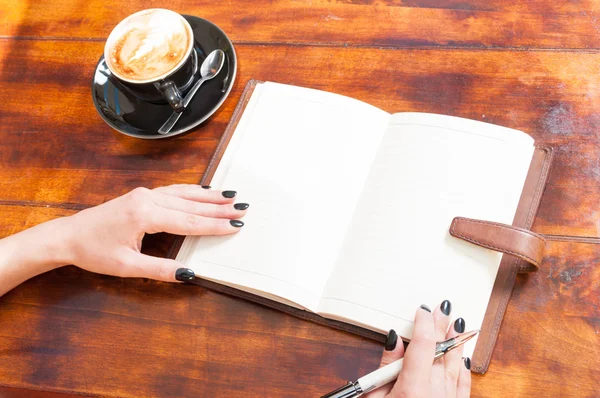 Woman hands with open notebook outside with coffee