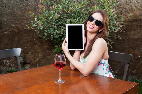 Woman showing tablet and having wine on terrace