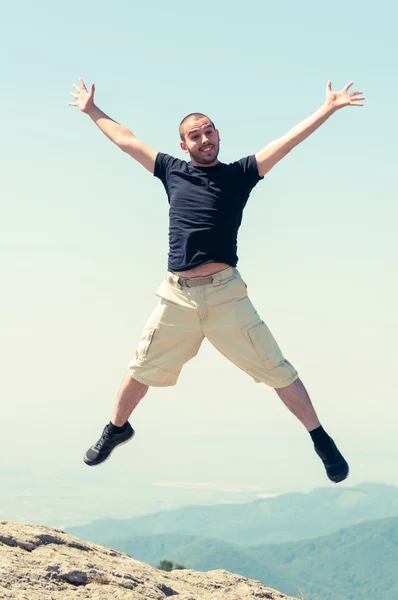 Happy man jumping on top of the mountain