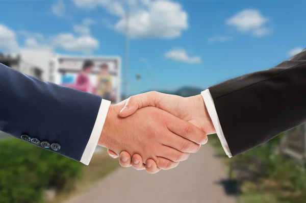 Real estate sale handshake over land and sky background