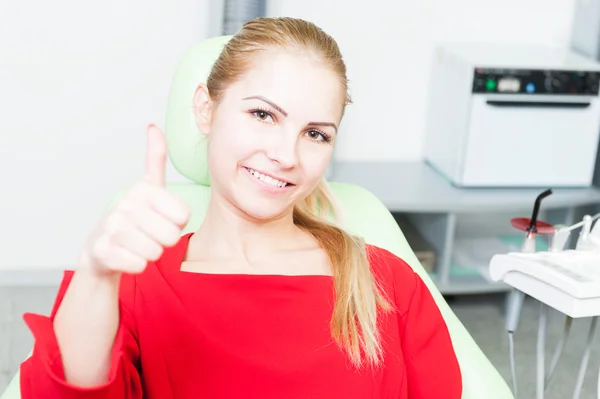 Happy female patient at dentist showing thumb-up