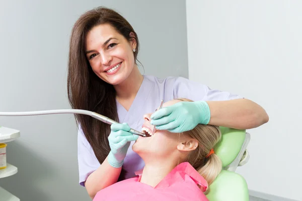 Friendly female dentist drilling patient tooth