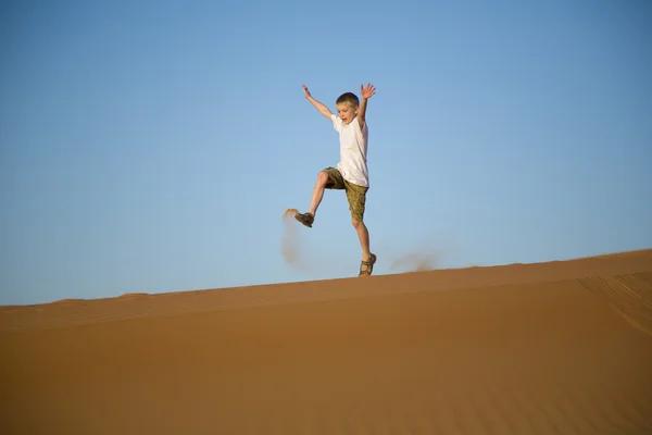 Little boy runs, jumps, plays on top of a sand dune in desert