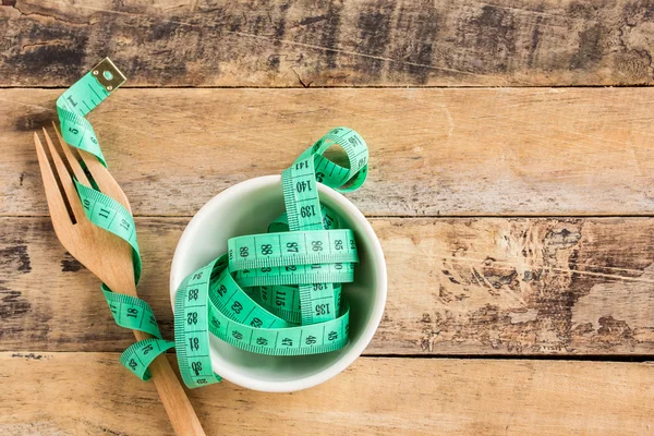 Green measuring tape in ceramic cup on wooden table