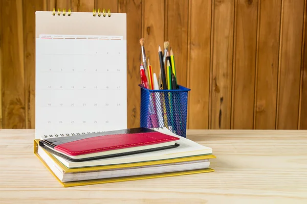 Note book,pen,pencil and stack of book with calendar on wooden t