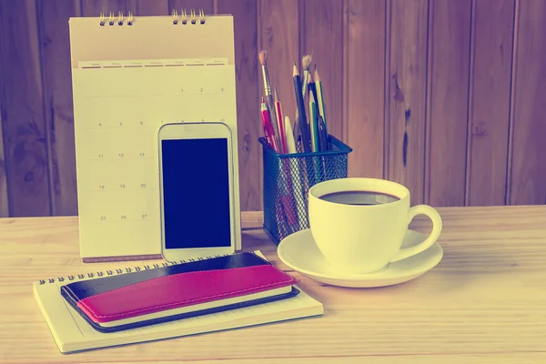 Note book,smart phone,coffee cup,and stack of book with calendar