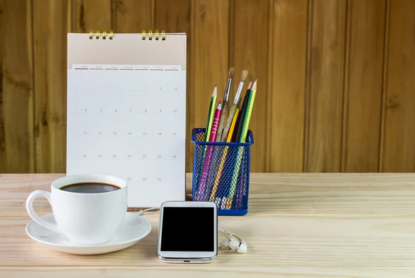 Smart phone,coffee cup,and calendar on wooden table background