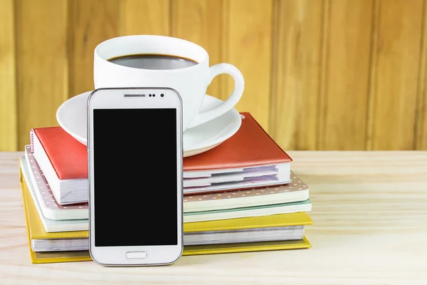 Smart phone, coffee and note book on wood table background.