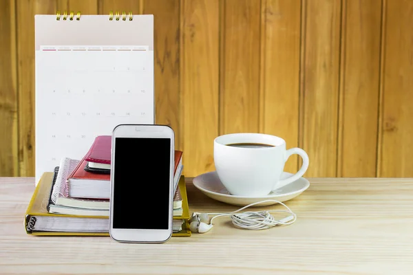 Smart phone,coffee cup,and stack of book with calendar on wooden