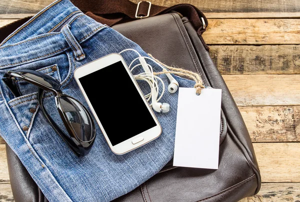 Brown leather bag,blue jean,smart phone and earphone on wooden t